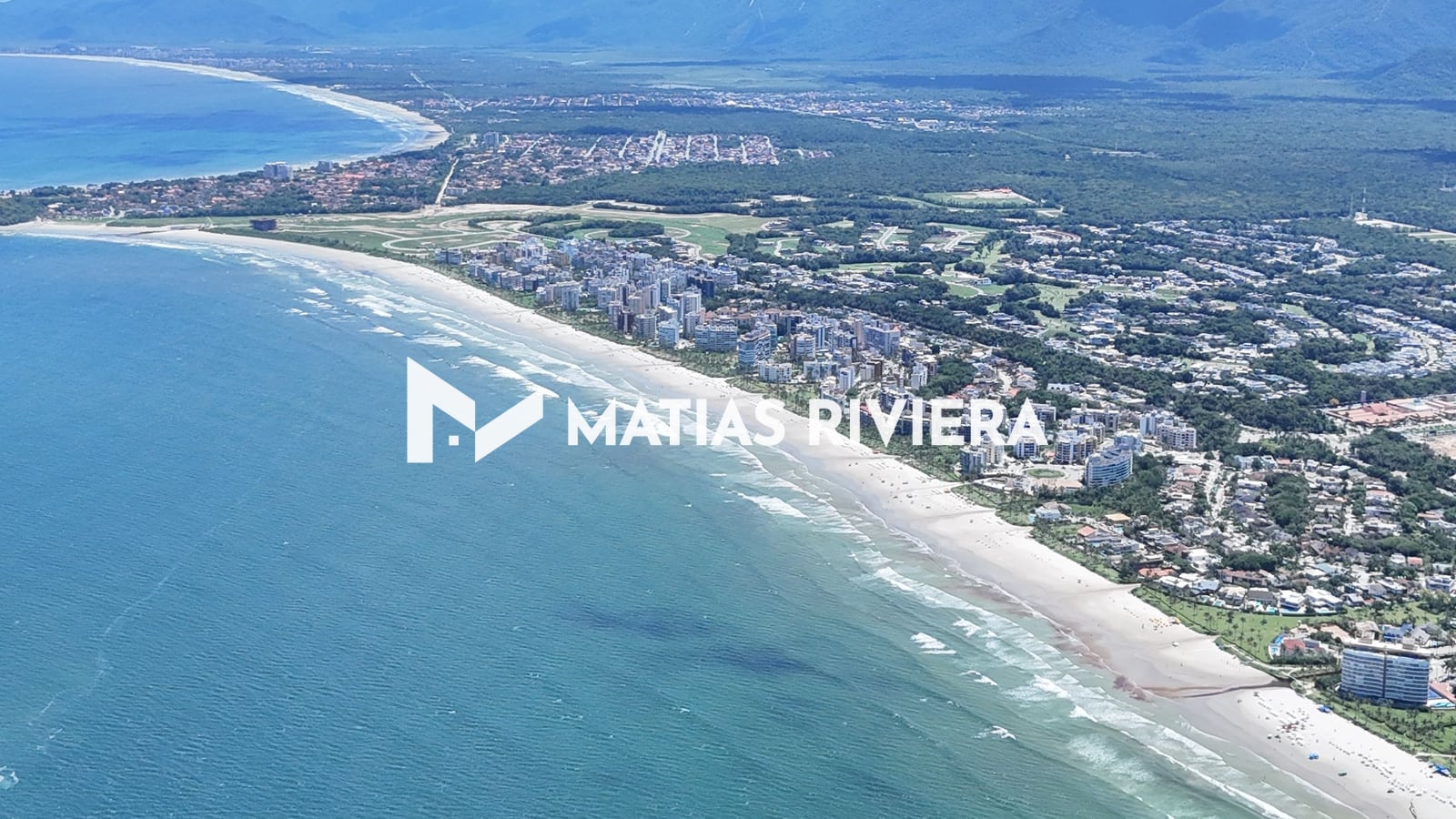 Baía da Riviera de São Lourenço vista do alto, com mar azul, a praia em curva e a serra ao fundo