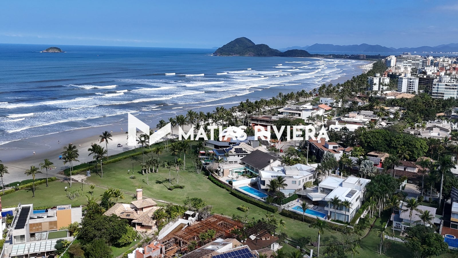 Casas entre palmeiras e gramado junto à praia da Riviera de São Lourenço, com o morro e as ilhas ao fundo
