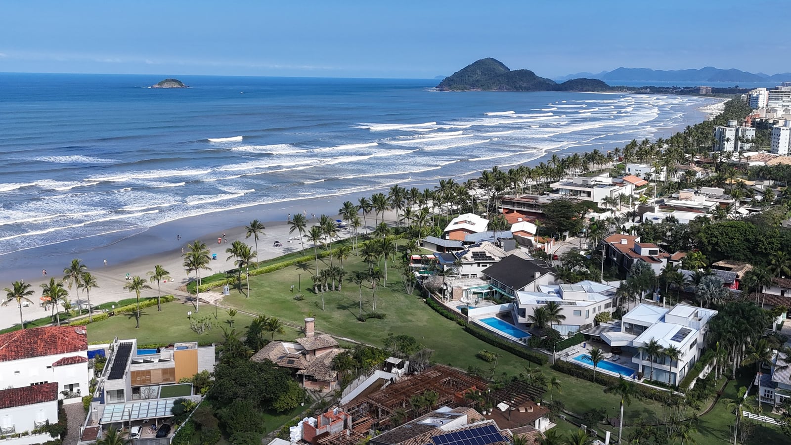 Casas e palmeiras à beira da praia da Riviera de São Lourenço, com o mar e o morro no horizonte
