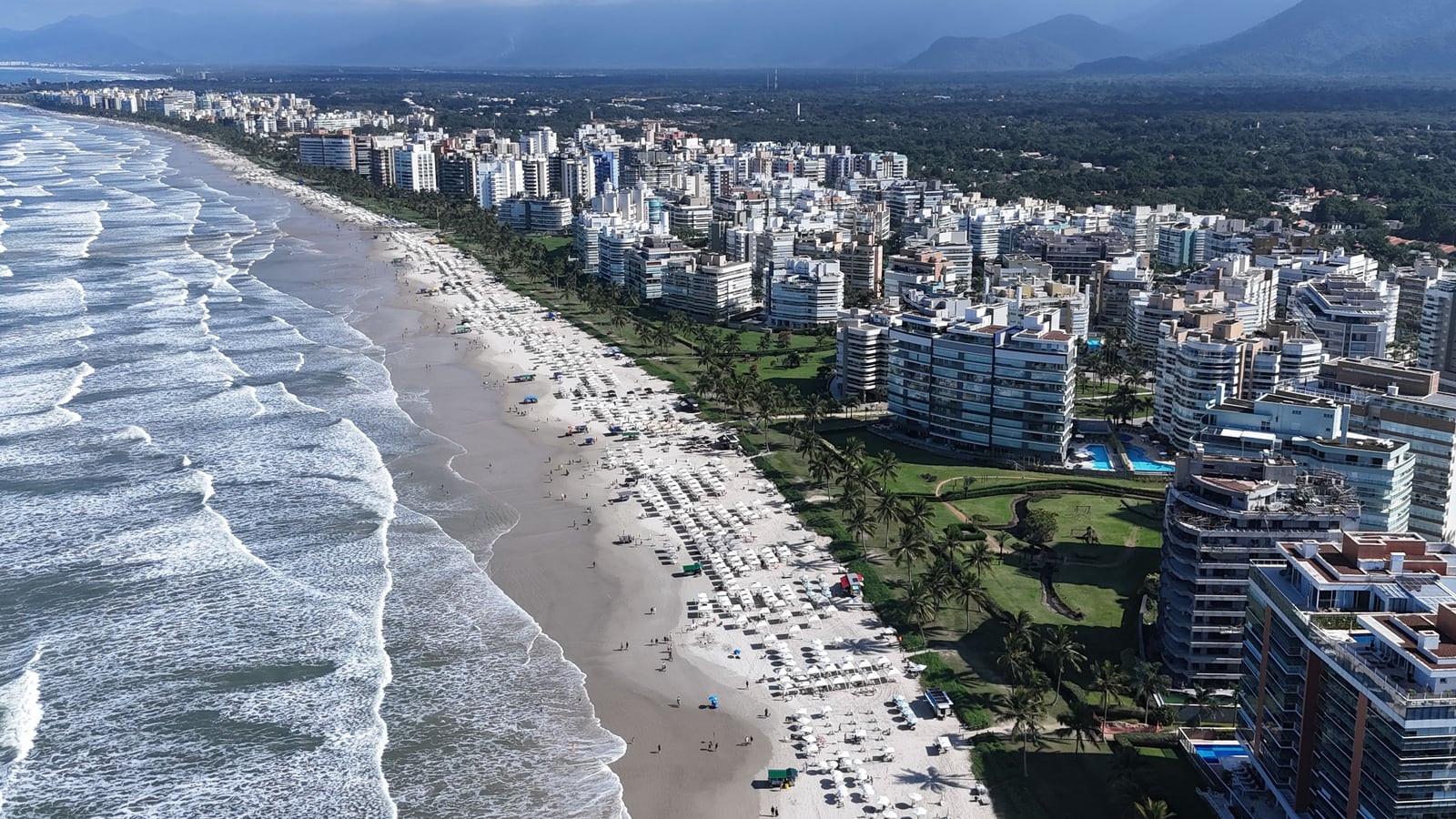 Ondas, areia e edifícios da orla da Riviera de São Lourenço vistos do alto em dia de sol