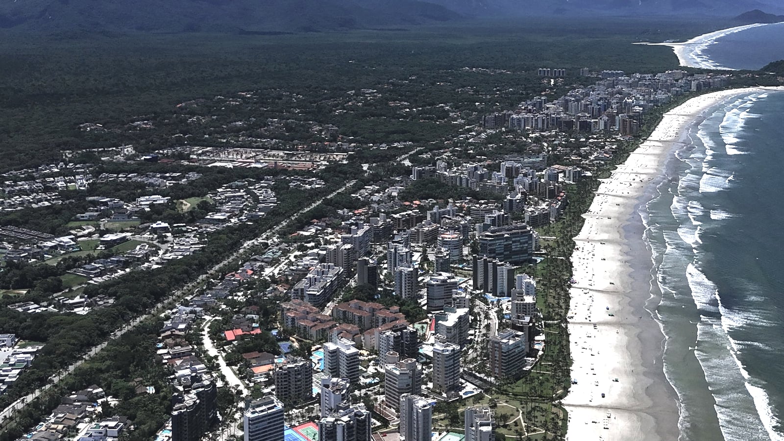 Vista aérea da Riviera de São Lourenço e da praia, com o morro na ponta e a Serra do Mar ao fundo