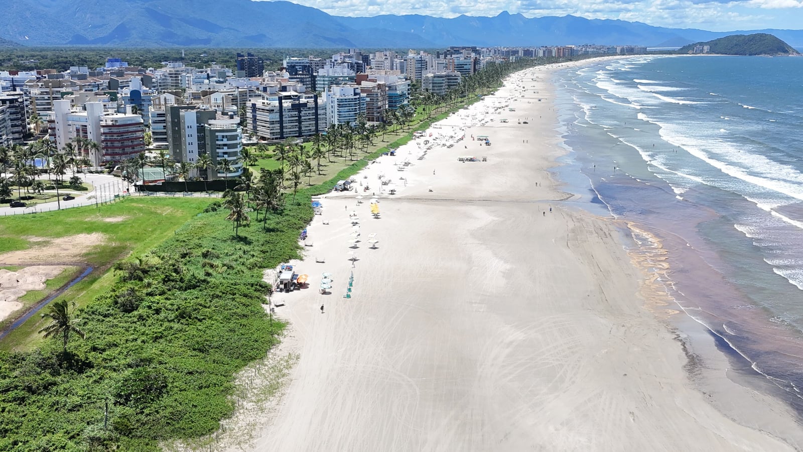 Faixa de areia e restinga da Riviera de São Lourenço vistas do alto, com os edifícios da orla e a serra ao fundo