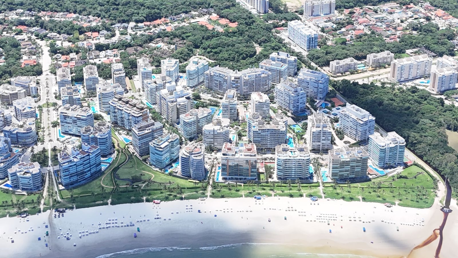A ponta da orla da Riviera de São Lourenço vista do alto, com edifícios, mata e a praia