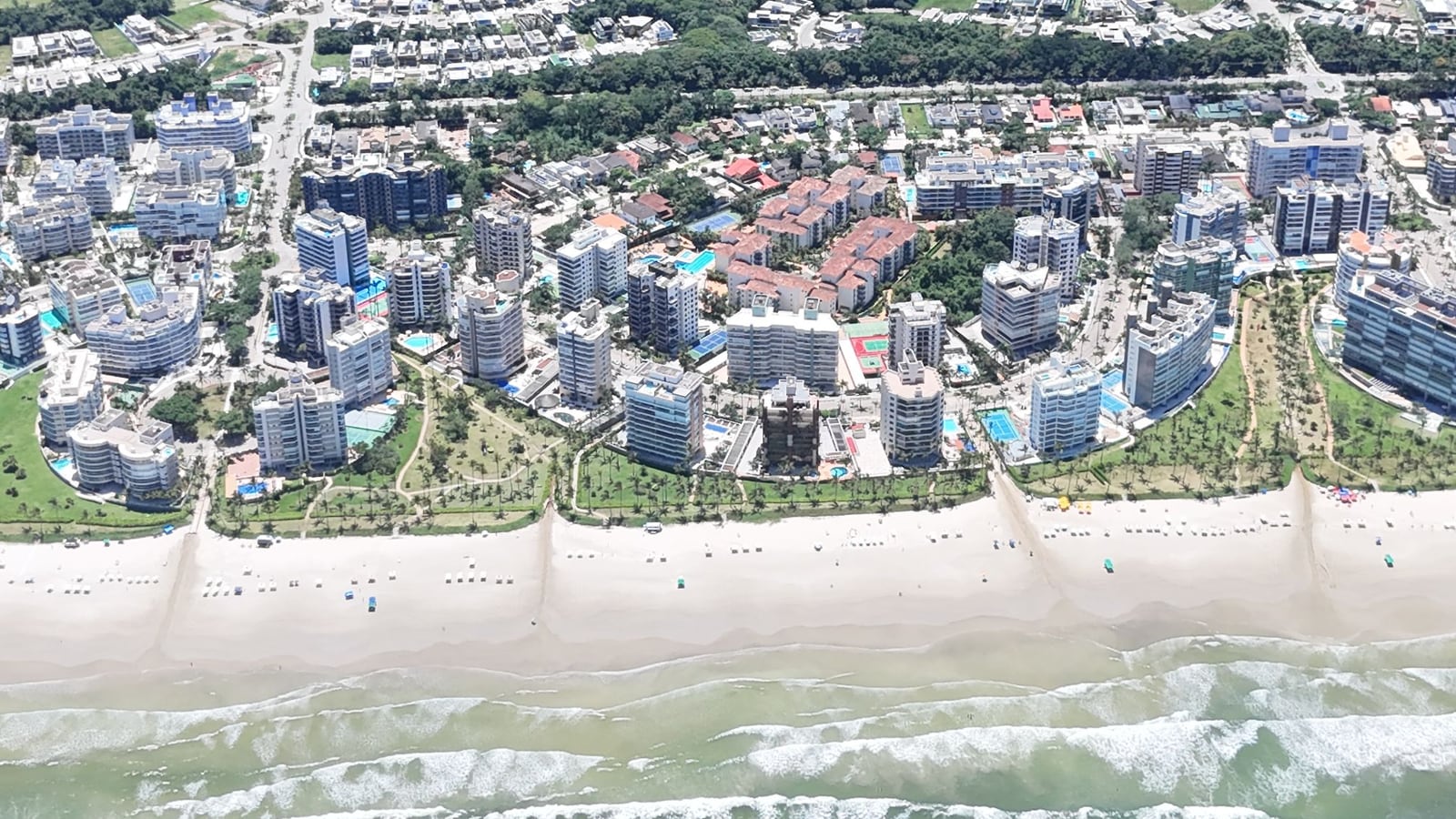 Praia, edifícios da orla e módulos residenciais da Riviera de São Lourenço vistos do alto, com a mata ao fundo