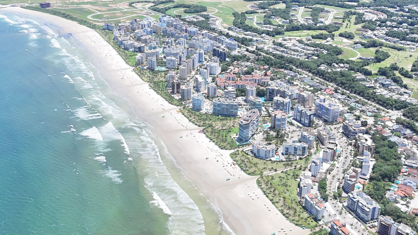 Praia e edifícios da Riviera de São Lourenço vistos do alto, com o mar azul e as áreas verdes