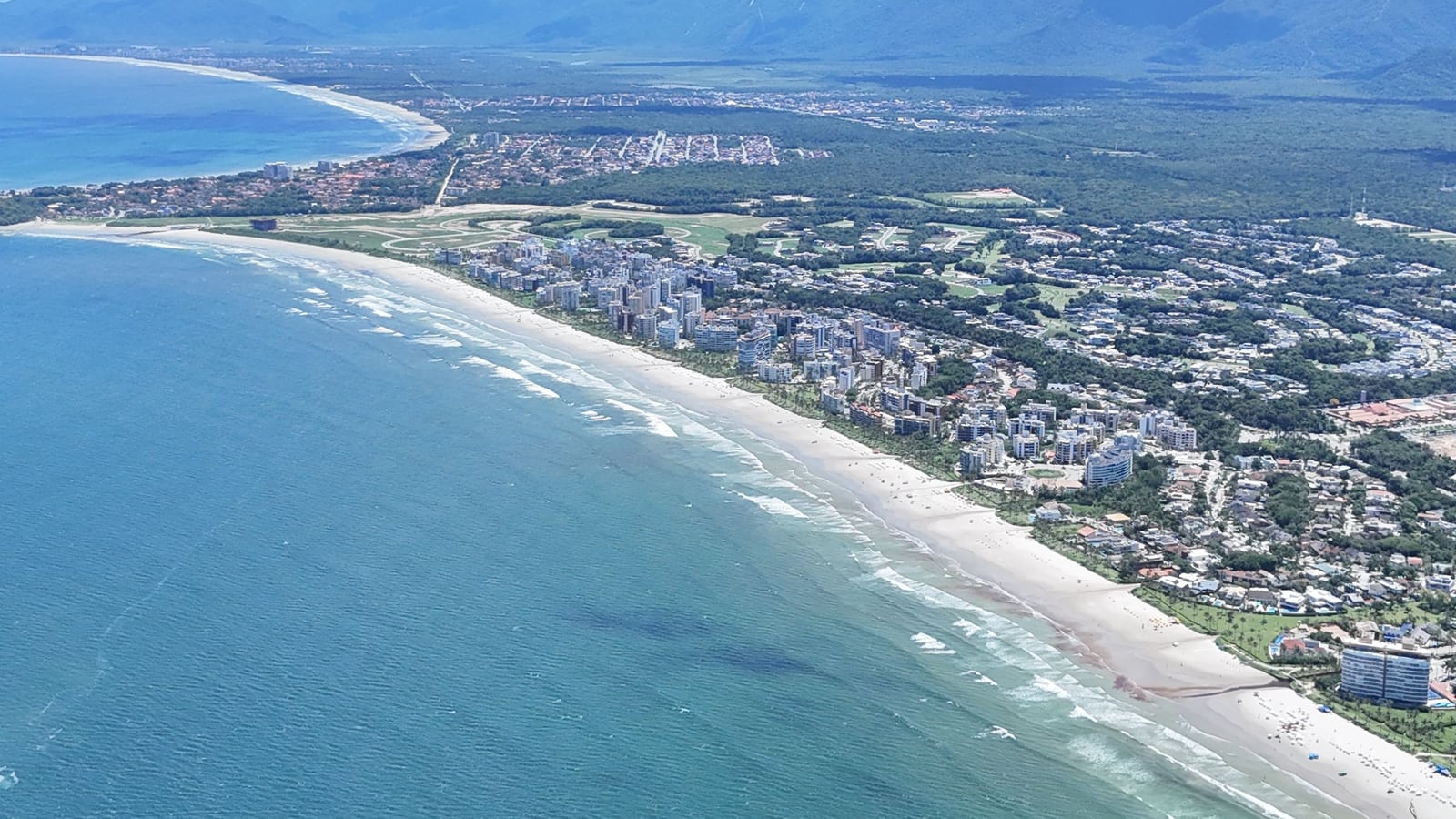 Baía da Riviera de São Lourenço vista do alto, com mar azul, a praia em curva e a serra ao fundo