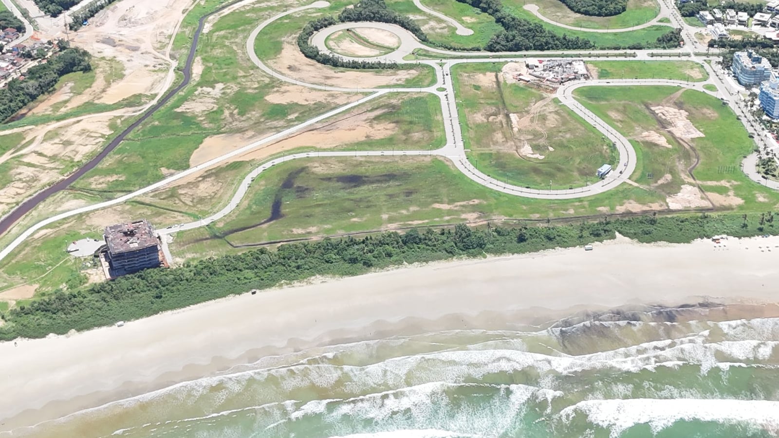 Praia e módulos da Riviera de São Lourenço vistos do alto, com áreas verdes e ruas em curva até a mata