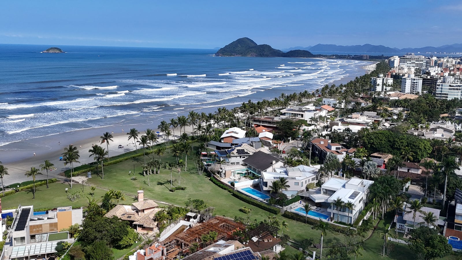 Casas entre palmeiras e gramado junto à praia da Riviera de São Lourenço, com o morro e as ilhas ao fundo