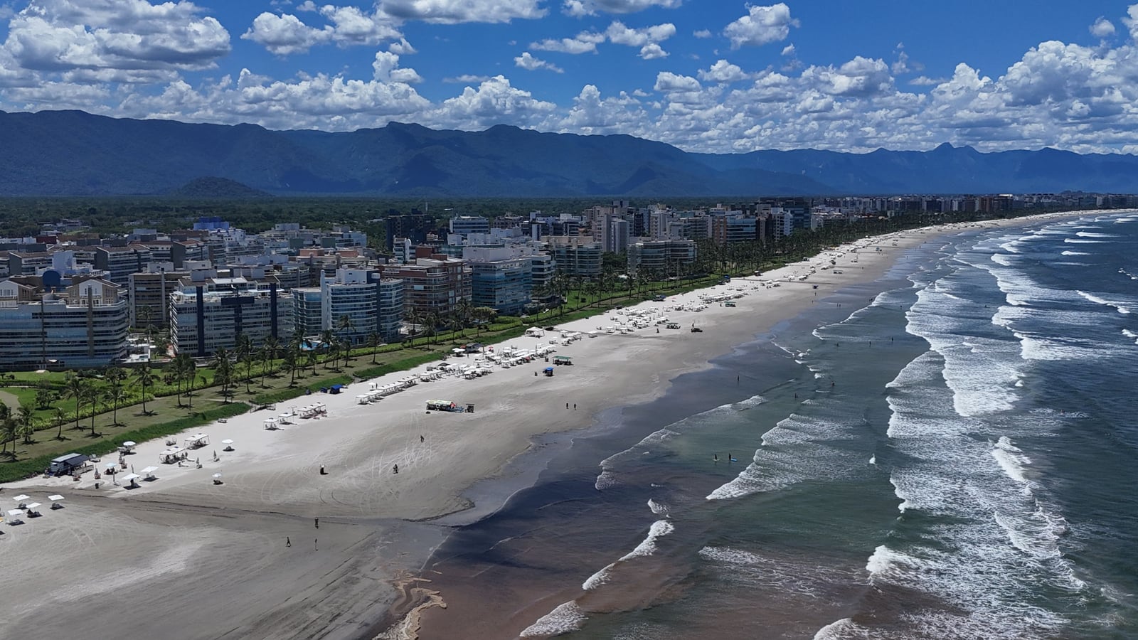 Orla da Riviera de São Lourenço vista do alto: faixa de areia larga, ondas e edifícios da beira-mar sob céu azul